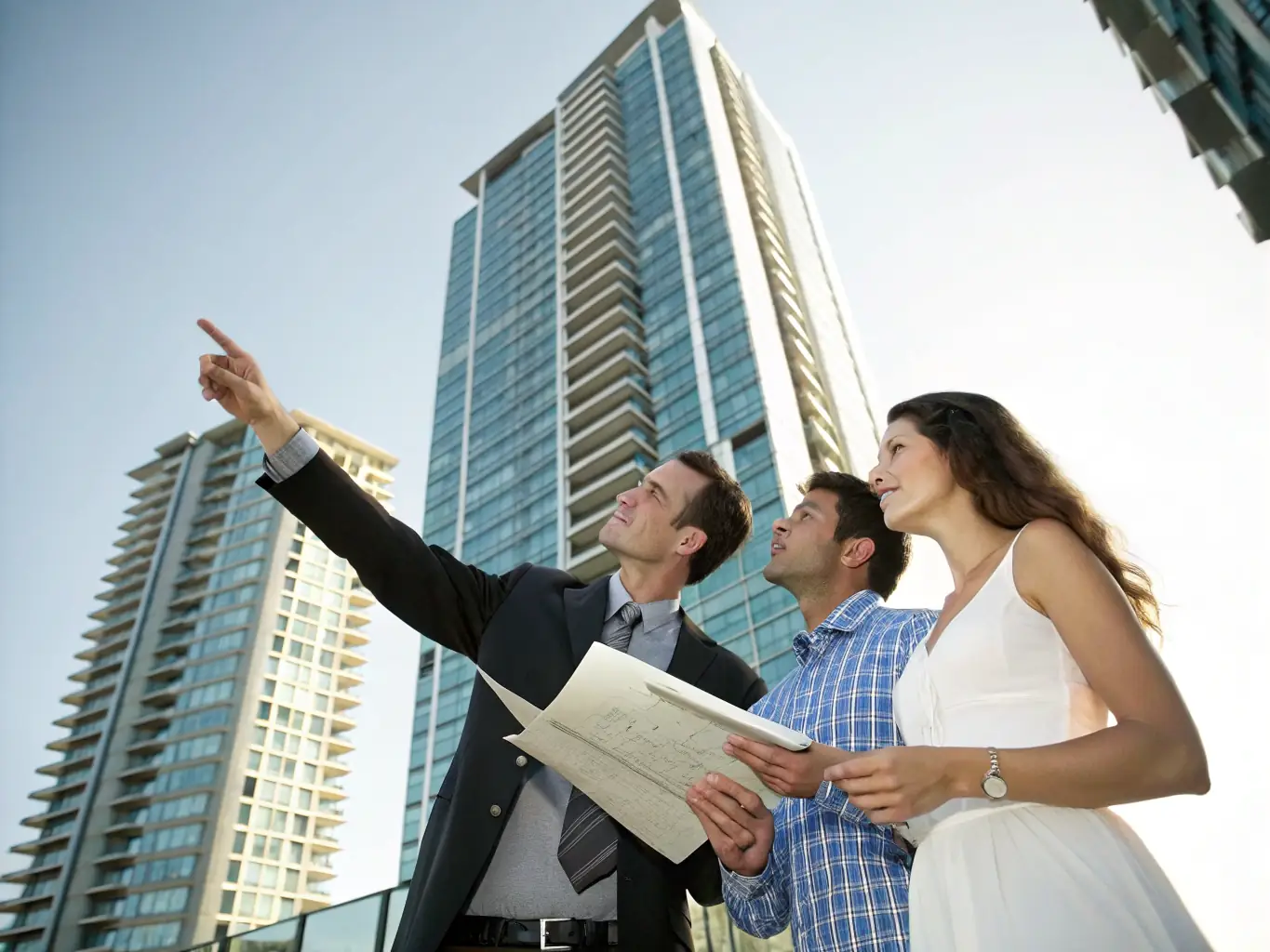 An image of a modern residential building with a real estate agent showing property plans to clients. The setting is bright and professional, highlighting the potential for profitable real estate investments.